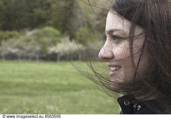 A young woman in profile. Her brown hair blowing about her face. Outdoors. Spring.