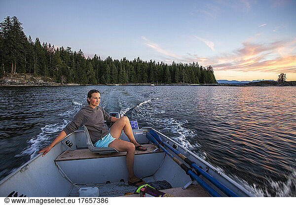 A young woman in steers a small boat at sunset