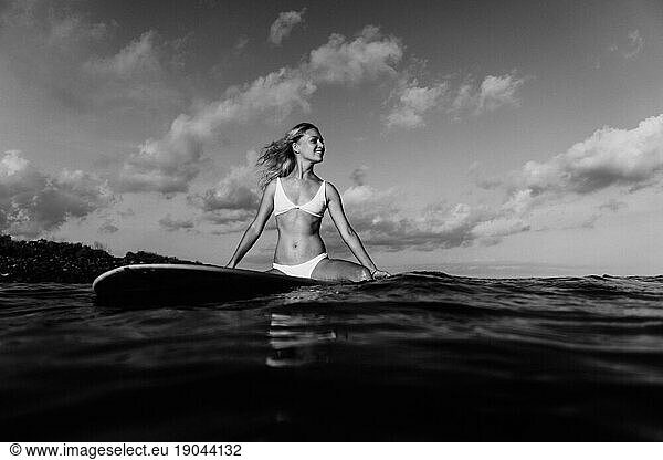 A young woman is sitting on a surfboard in the ocean.