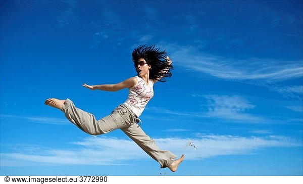 A young woman jumps in Australia beach againts a blue sky.
