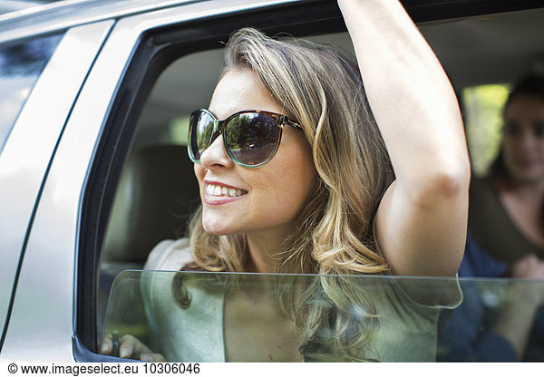 A young woman leaning out of a car window with her arm raised.