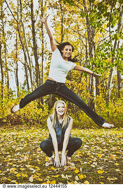 A young woman leaping high in the air over her friend in a park during the fall season  Edmonton  Alberta  Canada