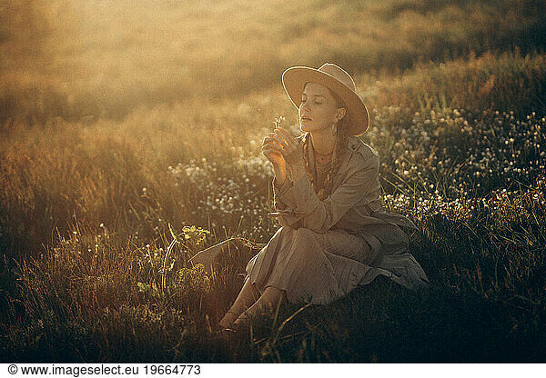 A young woman meets the sunset in the summer in a field