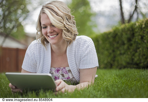 A young woman reading using a handheld electronic device  or e reader.