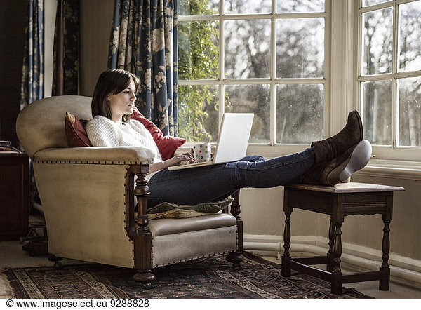 A young woman relaxing at home  with her feet up  using a laptop.