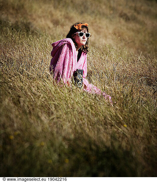 A young woman sitting in a field holding a camera. California  United States.
