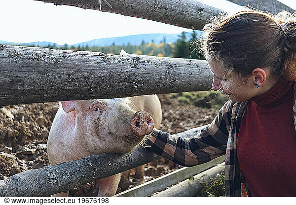 A young woman smiles at a pig and strokes it