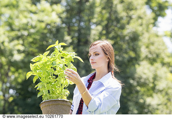 A young woman standing in a garden tending a plant in a pot.