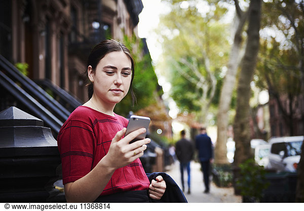 A young woman standing on a city street looking at a cellphone.