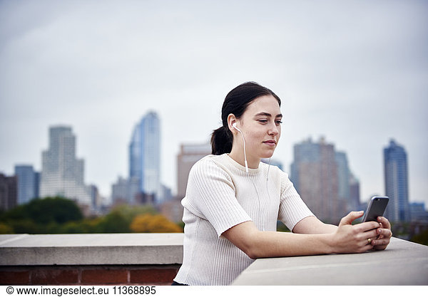 A young woman standing on a rooftop looking at a cellphone.