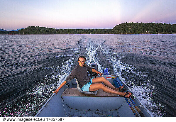 A young woman steers a small boat at sunset