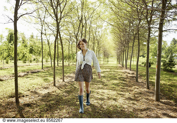 A young woman walking down an avenue of trees in woodland.