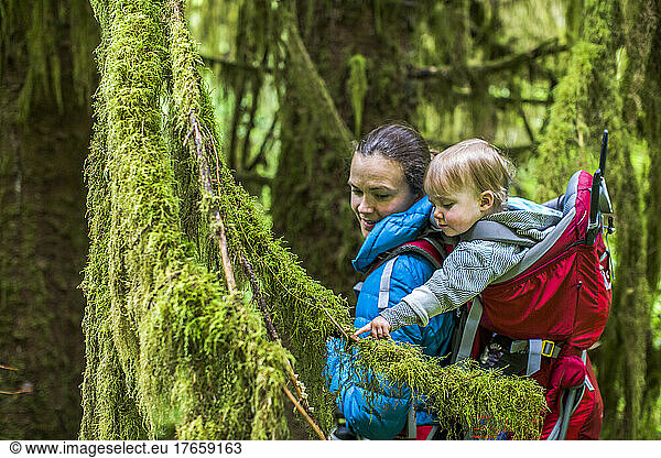 A young woman walks in forest with a baby in a backpack