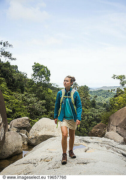 A young woman walks on a rock overlooking the jungle of Puerto Rico.