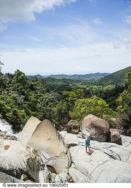 A young woman walks on a rock overlooking the jungle of Puerto Rico.
