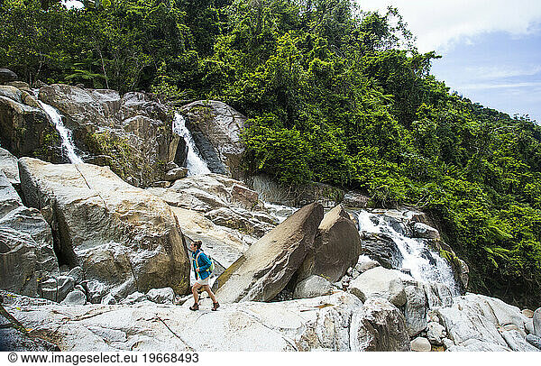 A young woman walks on a rock overlooking the jungle of Puerto Rico.