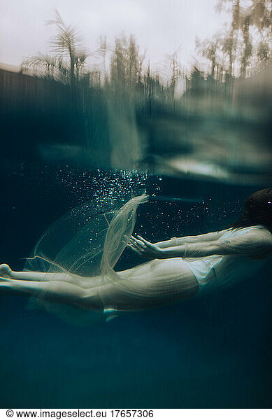 A young woman wearing a dress swimming underwater