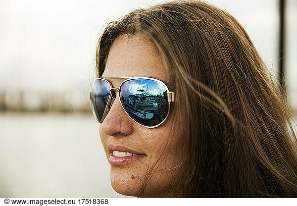 A young woman with long hair wearing sunglasses reflects blue scenery