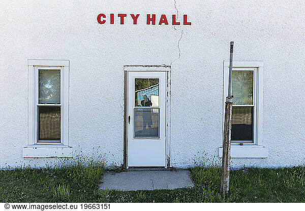 Abandoned City Hall building  sign  door and windows  reflection of a photographer in the glass.