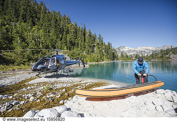 Abenteuerlustiger Mann pumpt aufblasbaren SUP neben einem abgelegenen See auf.