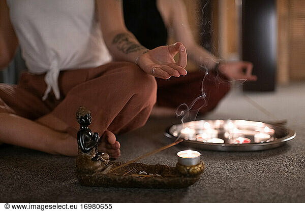 Abgeschnittene Frau meditiert neben Weihrauch und Kerzen
