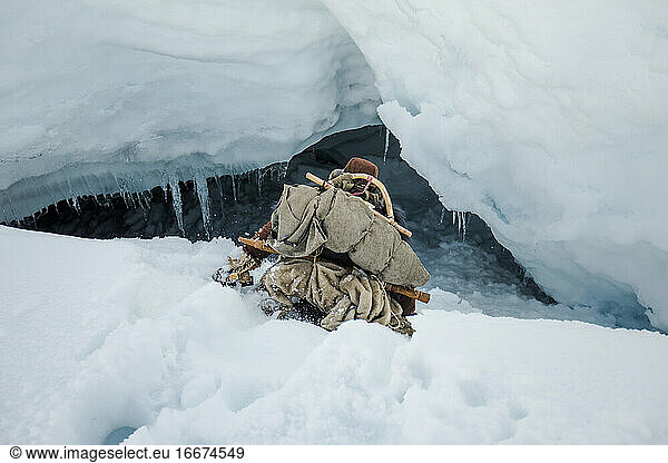 Aboriginal explorer slides down into a ice cave entrance.