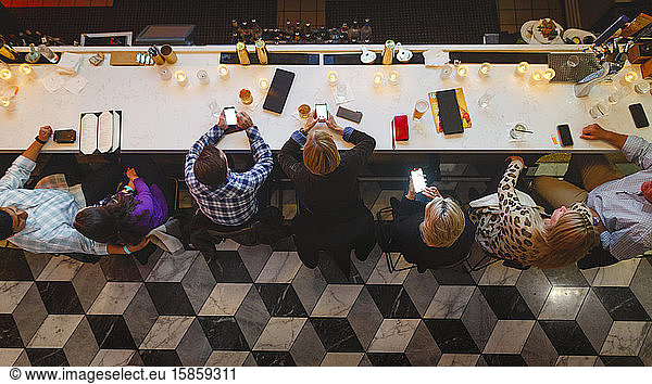 Above-view of a line of people at a bar looking at their cell phones