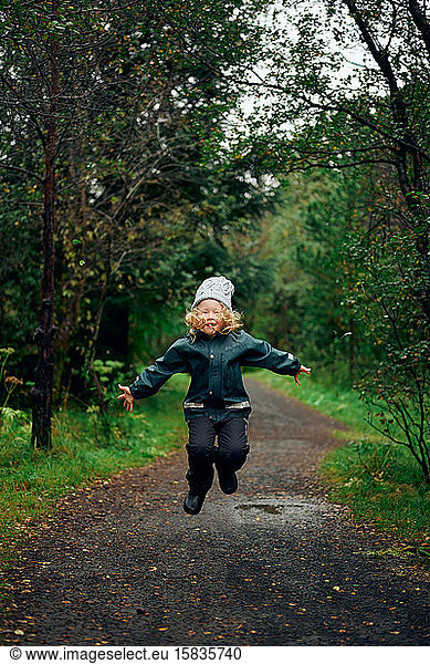 Active kid jumping on forest wet road