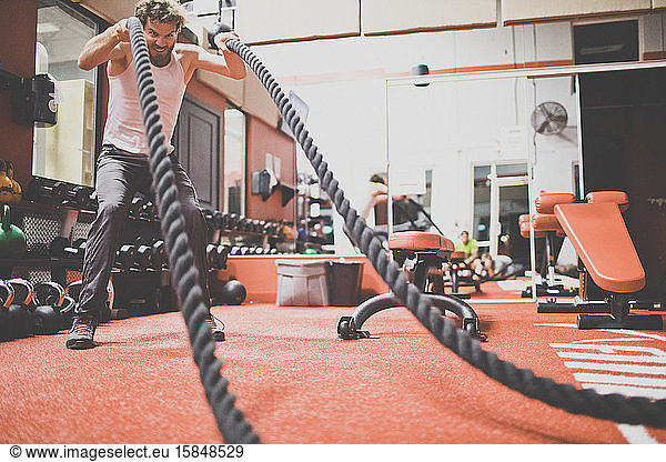 Active man exercising with battling rope at fitness club