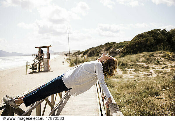 Active mature woman balancing on boardwalk at beach
