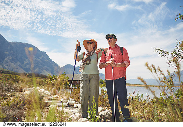 Active senior couple hiking with hiking poles at sunny summer lakeside