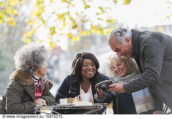 Active senior friends using digital camera at autumn sidewalk cafe