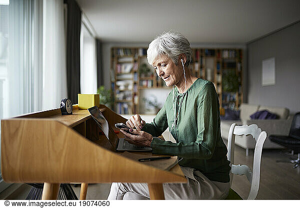 Active senior listening music while sitting on chair at home