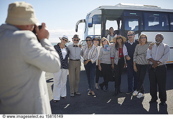 Active senior tourist friends posing for photograph outside tour bus