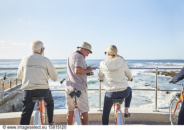 Active senior tourists on bicycles looking at sunny ocean view