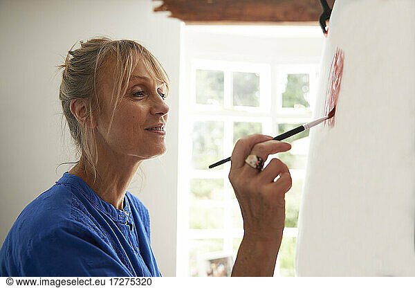 Active senior woman concentrating while painting on canvas at home