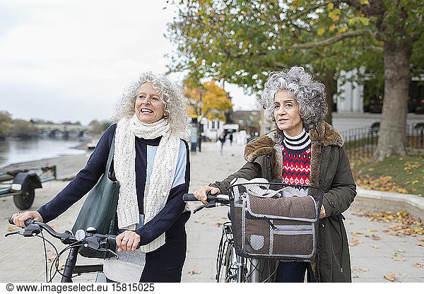 Active senior women friends walking bicycles in autumn park