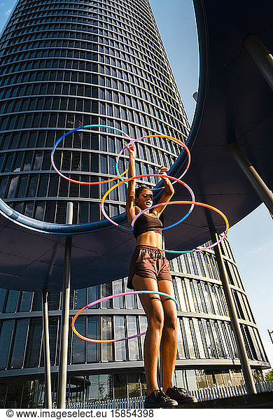 Active woman performing Hula Hoop dance with five rings in urban area