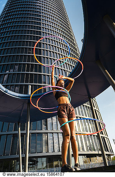 Active woman performing Hula Hoop dance with five rings in urban area