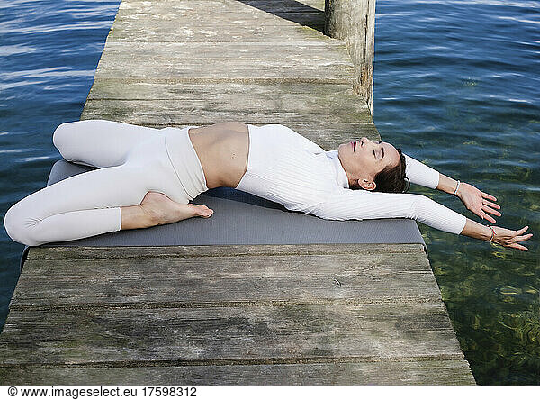 Active woman practicing yoga on jetty at lake