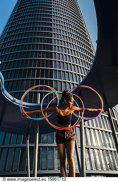 Active young woman holding five Hula Hoop in downtown at sunset