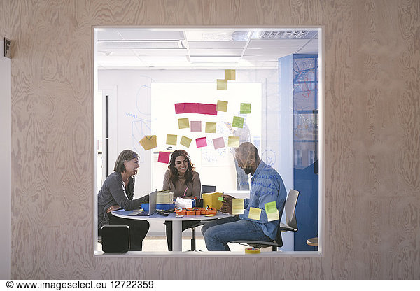 Adhesive notes stuck on glass with business professionals working in background