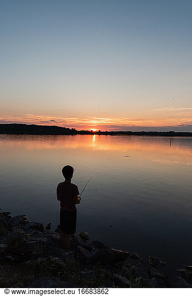 Adolescent boy fishing on shore of lake at sunset in Ontario  Canada.