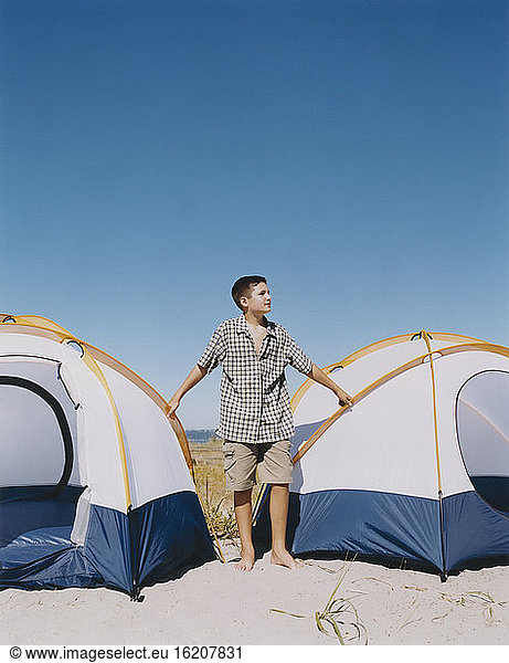 Adolescent boy standing by camping tents on beach