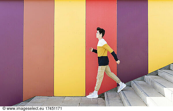 Adolescent going down stairs outdoor against colored wall