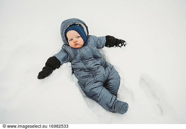 Adorable Baby looking sad lying on snow wearing a snowsui t