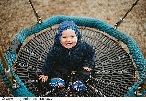 Adorable baby smiling at playground on hammock in cold winter