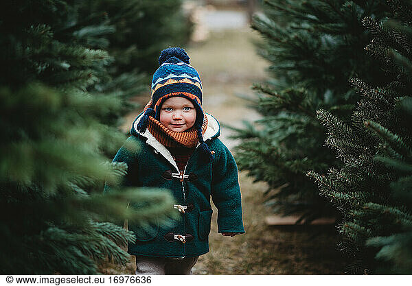 Adorable child wearing wool coat walking between Christmas trees