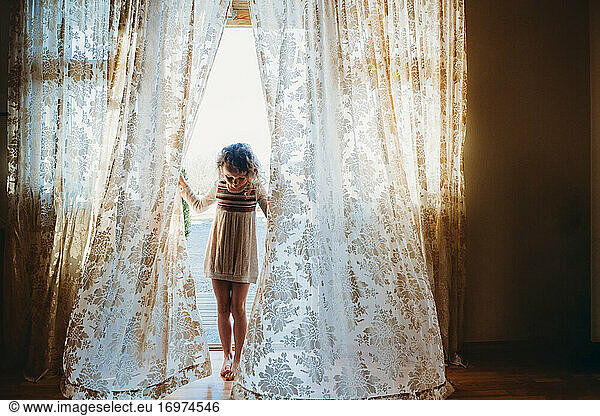 Adorable girl playing with vintage curtains at home during quarantine