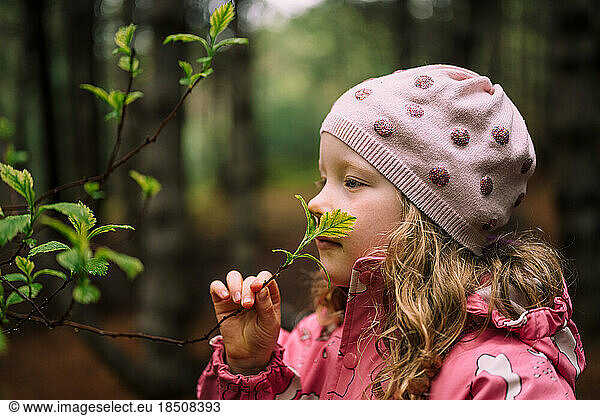 Adorable girl smelling branch in forest